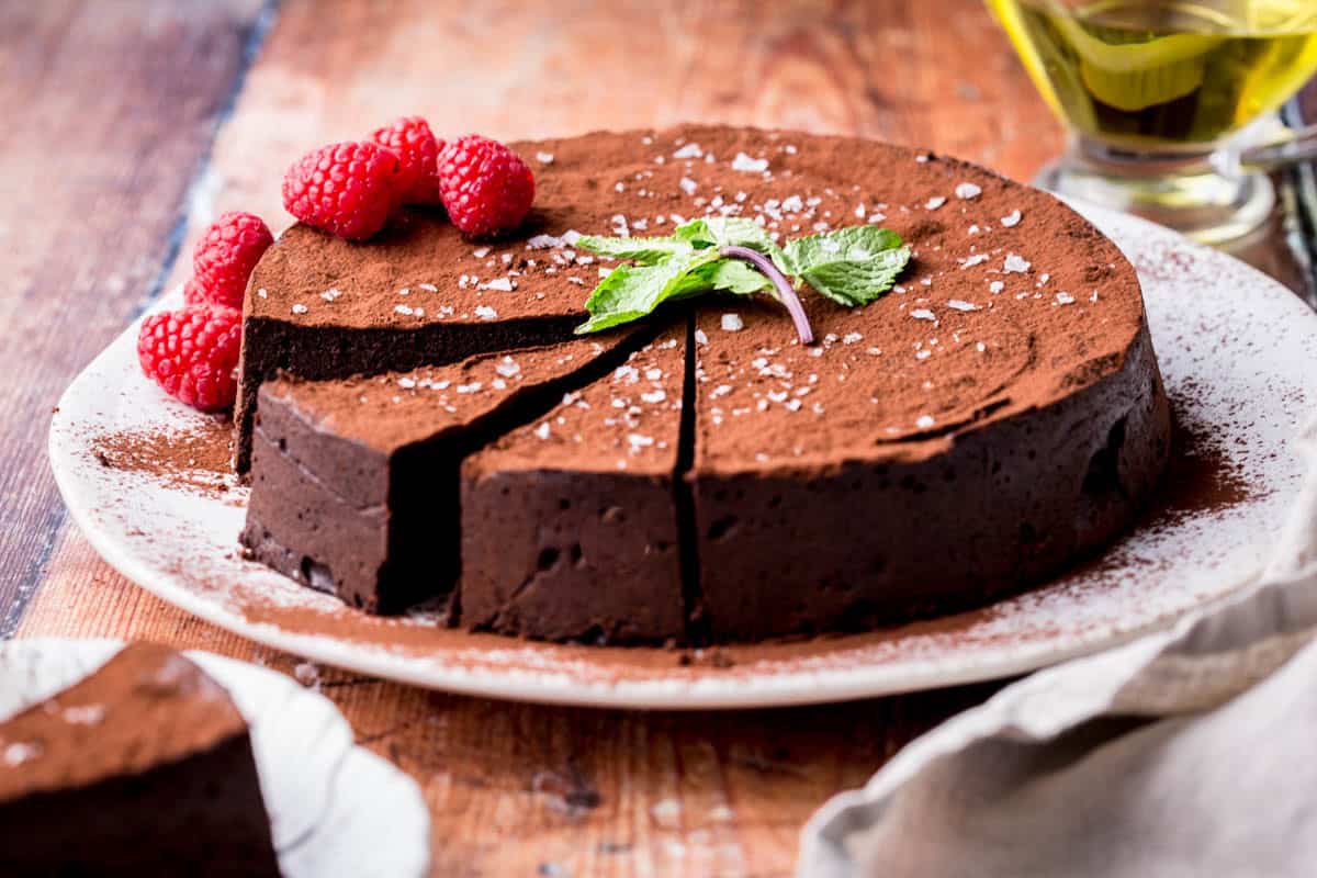 Sliced Flourless Olive Oil Chocolate Cake dusted with cocoa powder, sprinkled with flaky sea salt and decorated with a mint leaf and raspberries.