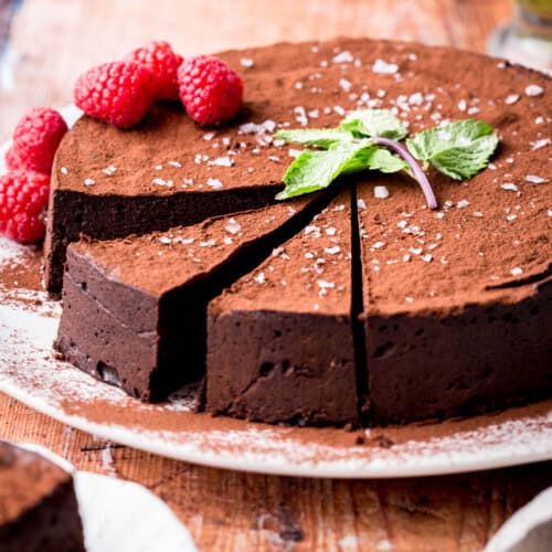 Sliced Flourless Olive Oil Chocolate Cake dusted with cocoa powder, sprinkled with flaky sea salt and decorated with a mint leaf and raspberries.