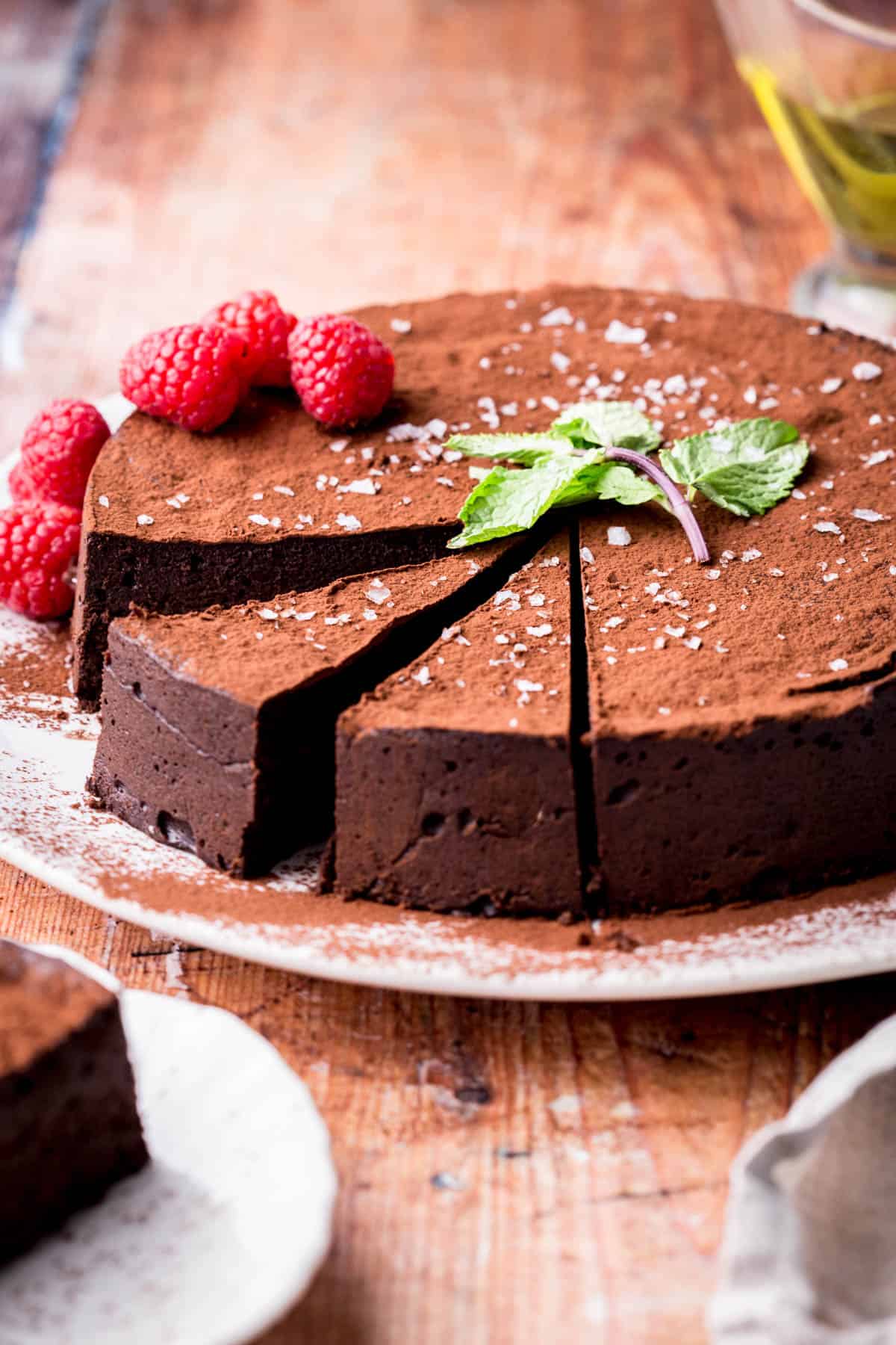 Sliced Flourless Olive Oil Chocolate Cake dusted with cocoa powder, sprinkled with flaky sea salt and decorated with a mint leaf and raspberries.