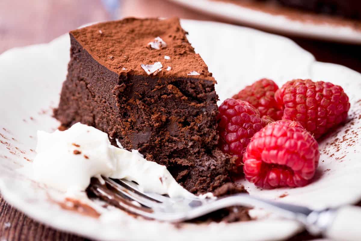 Flourless Olive Oil Chocolate Cake showing fudgy inside next to whipped cream and raspberries.