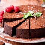 Sliced Flourless Olive Oil Chocolate Cake dusted with cocoa powder, sprinkled with flaky sea salt and decorated with a mint leaf and raspberries.