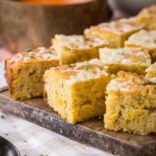 Sliced gluten-free cheddar chive cornbread on a serving board. Next to saucepan of hot soup, ready for serving.