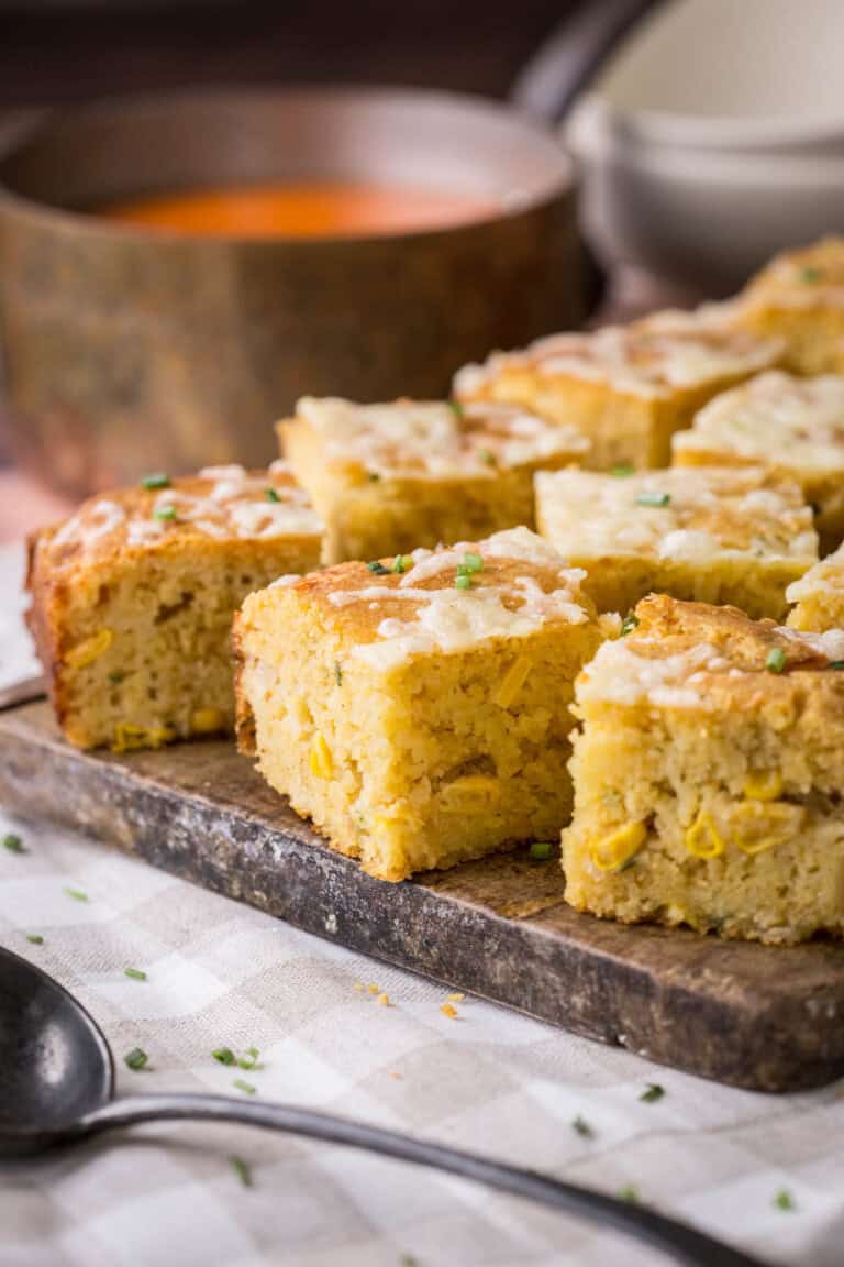 Sliced gluten-free cheddar chive cornbread on a serving board. Next to saucepan of hot soup, ready for serving.