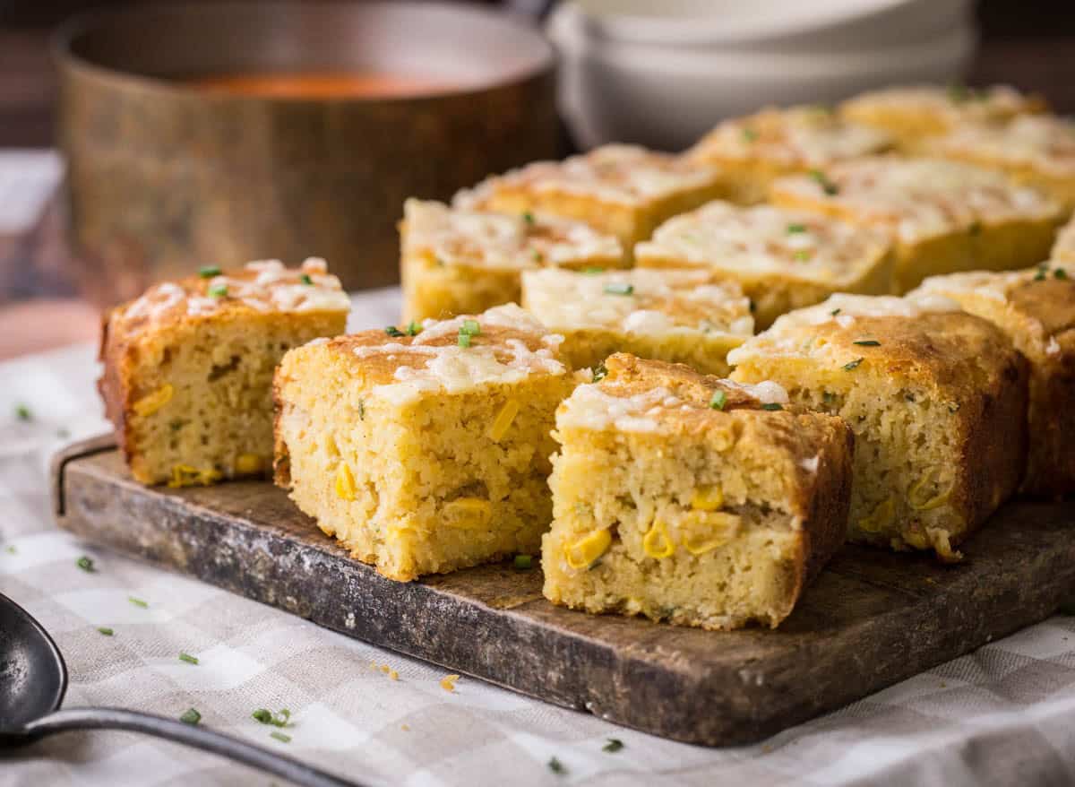 Sliced gluten-free cheddar chive cornbread on a serving board. Next to saucepan of hot soup, ready for serving.