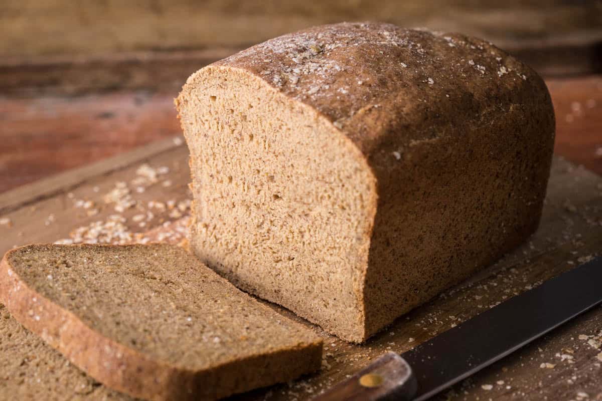 Loaf of gluten-free brown bread sliced on wooden board.