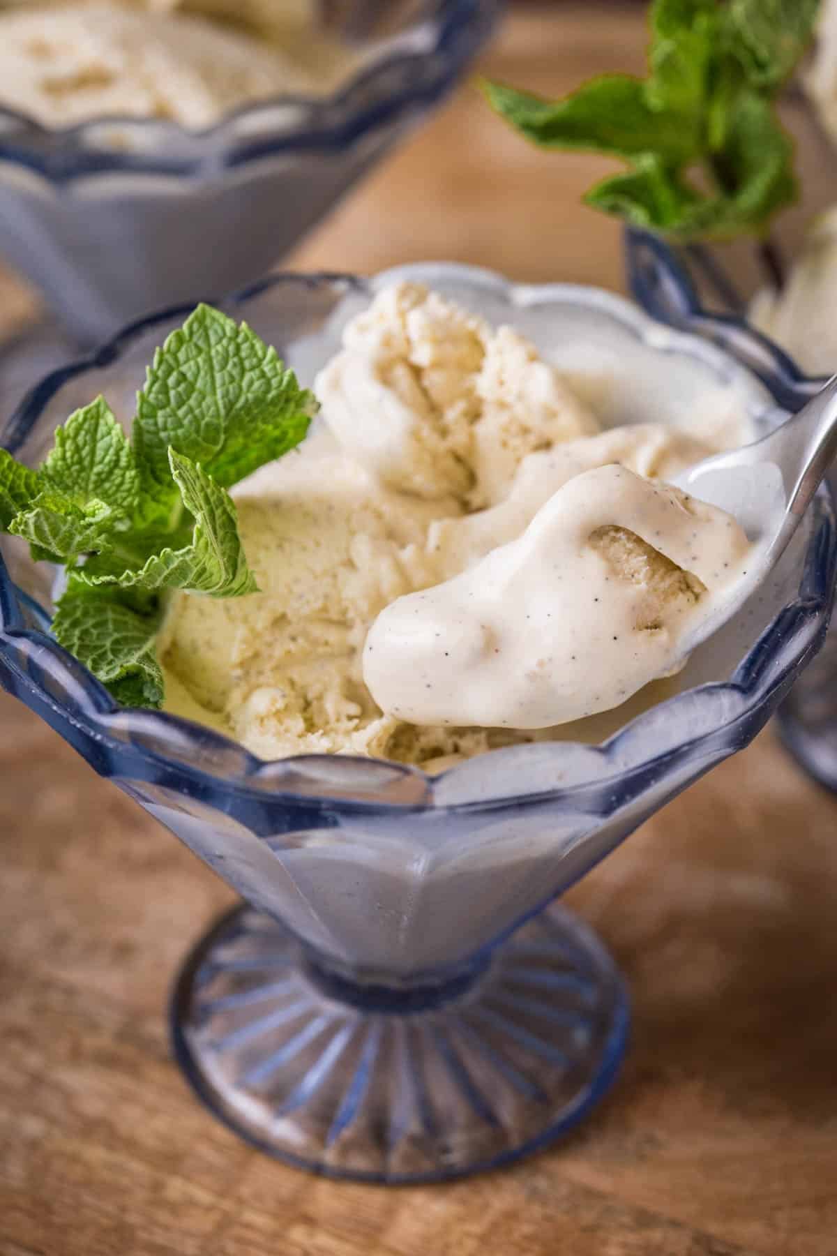 Melty and creamy Homemade Vanilla Ice Cream in a glass dish decorated with a sprig of mint.