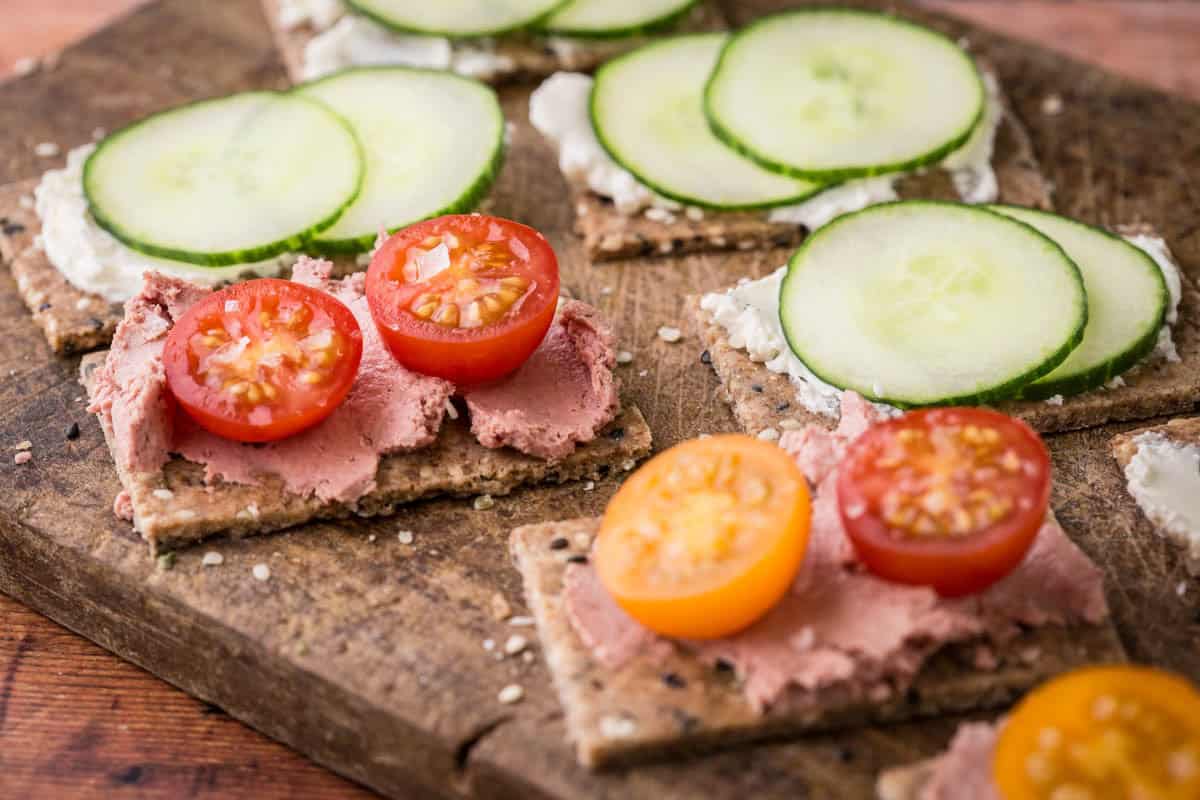 Seeded Gluten-Free Crispbreads spread with variety of toppings on wooden board.