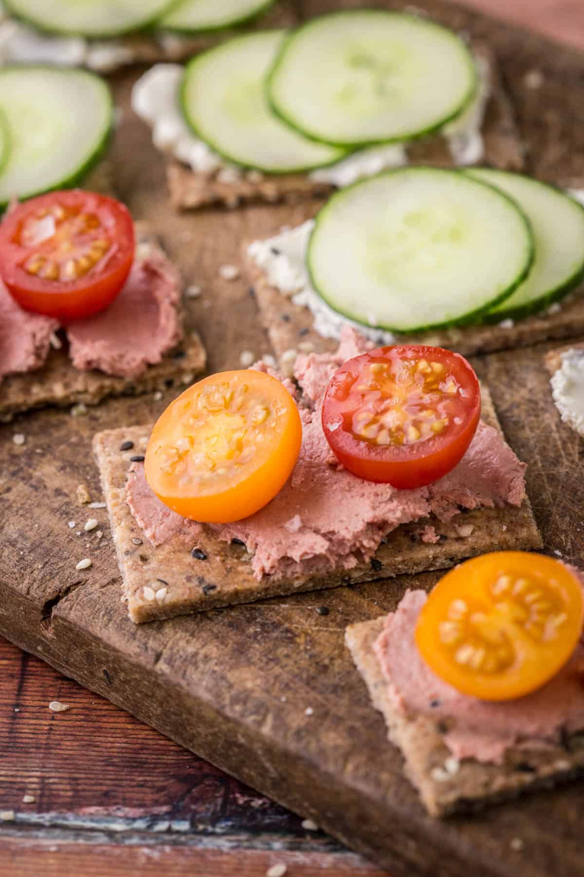 Seeded Gluten-Free Crispbreads spread with variety of toppings on wooden board.