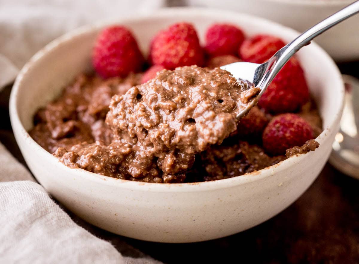 Spoon holding very creamy chocolate porridge coming out of a bowl.