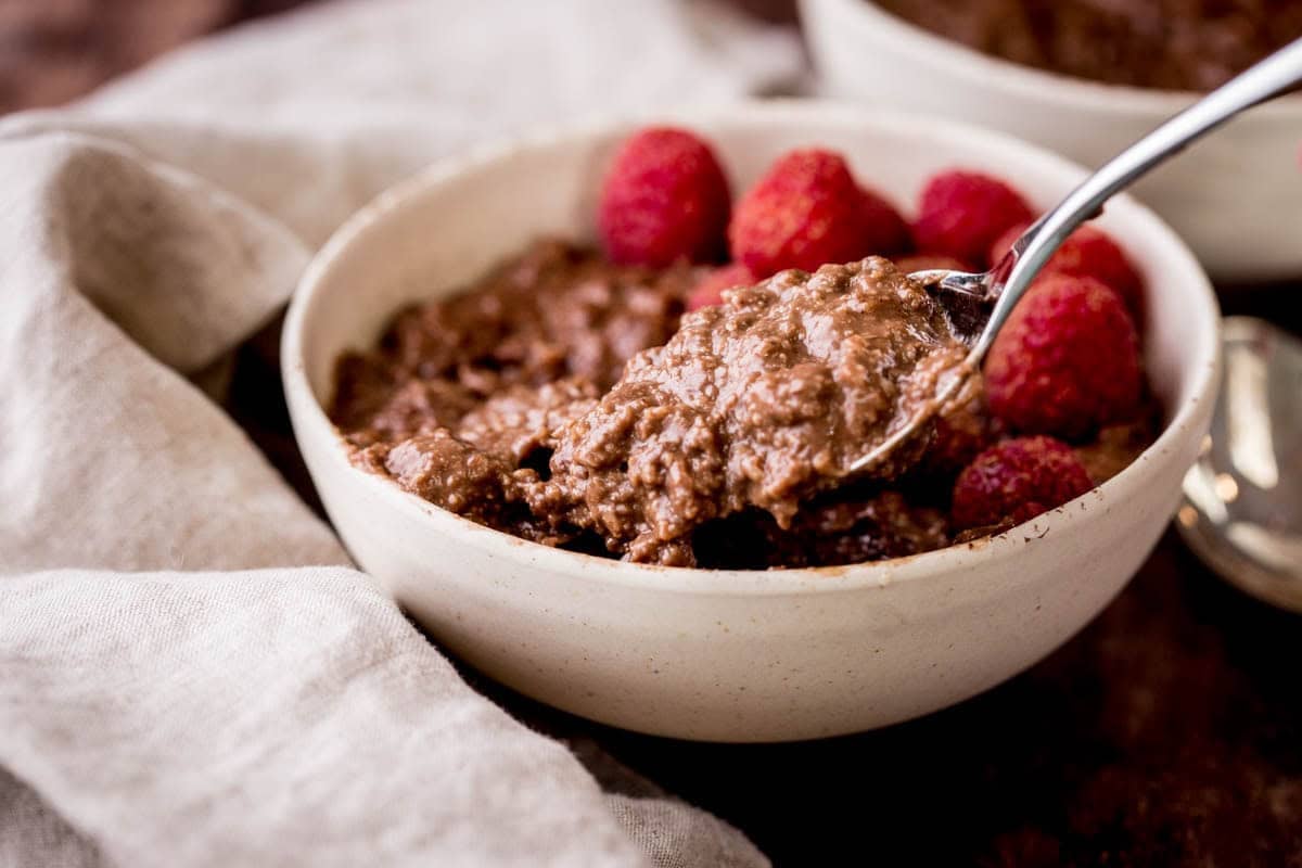 Spoon holding very creamy chocolate porridge coming out of a bowl.