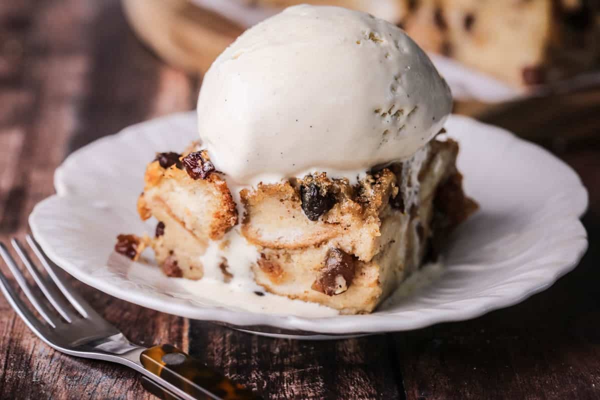 Slice of bread pudding on a plate with ice cream melting on top.