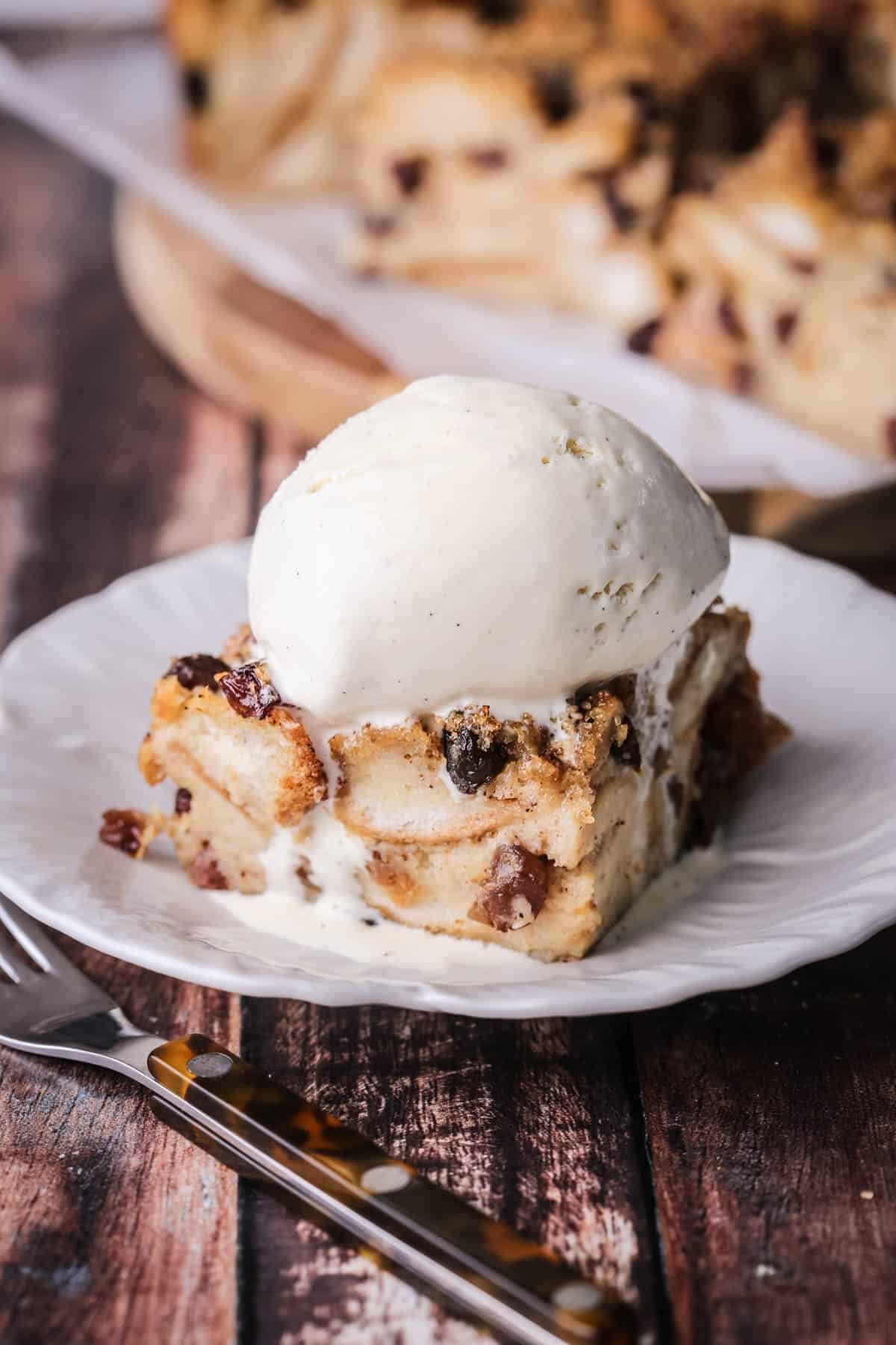 Slice of bread pudding on a plate with ice cream melting on top.