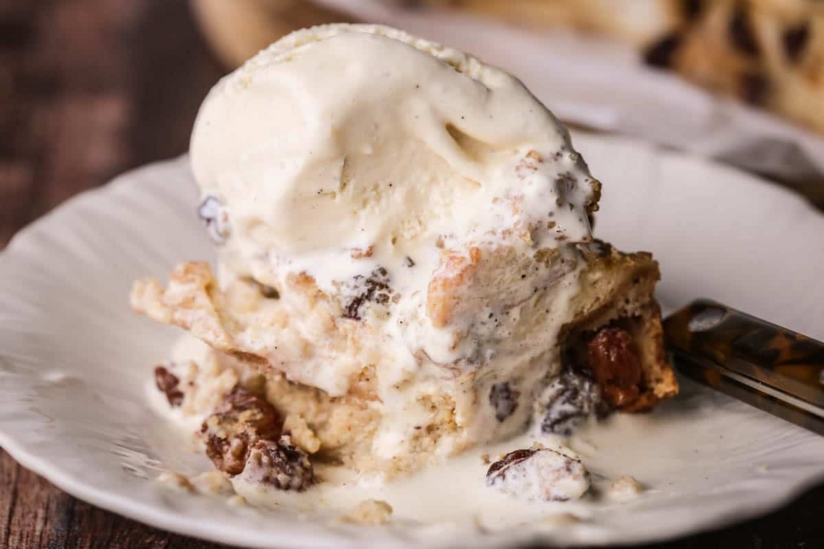 Slice of bread pudding on a plate with ice cream melting on top.