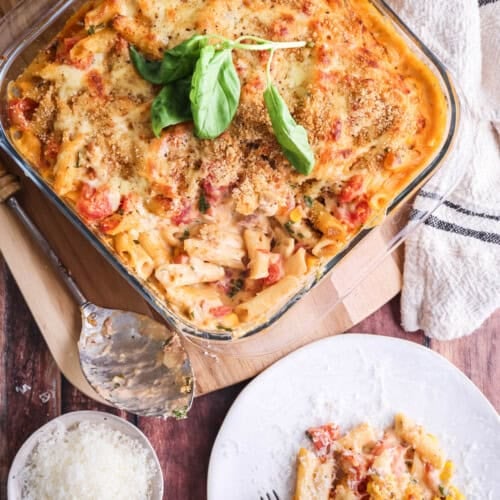 A dish of Gluten-Free Tuna Pasta Bake with a portion taken out showing creamy delicious inside. Portion sitting on a plate with extra cheese on top.