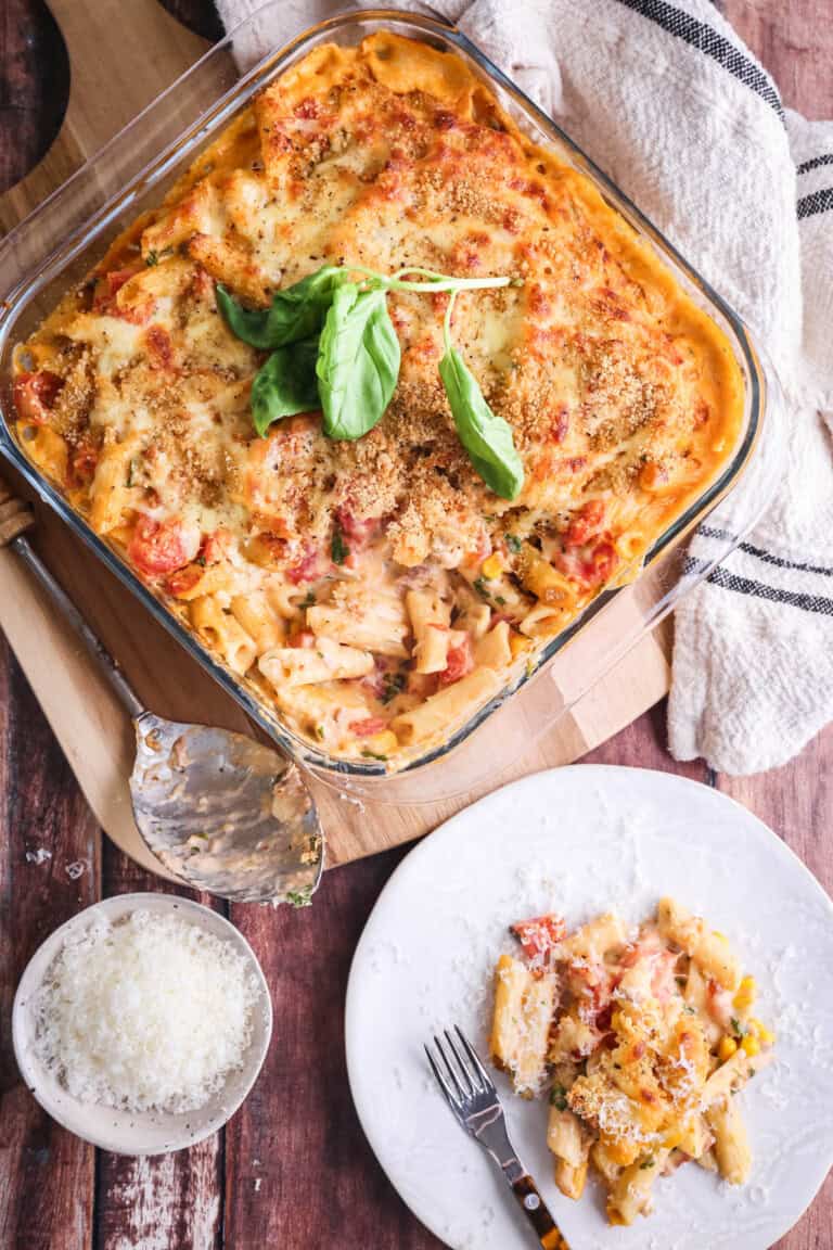 A dish of Gluten-Free Tuna Pasta Bake with a portion taken out showing creamy delicious inside. Portion sitting on a plate with extra cheese on top.