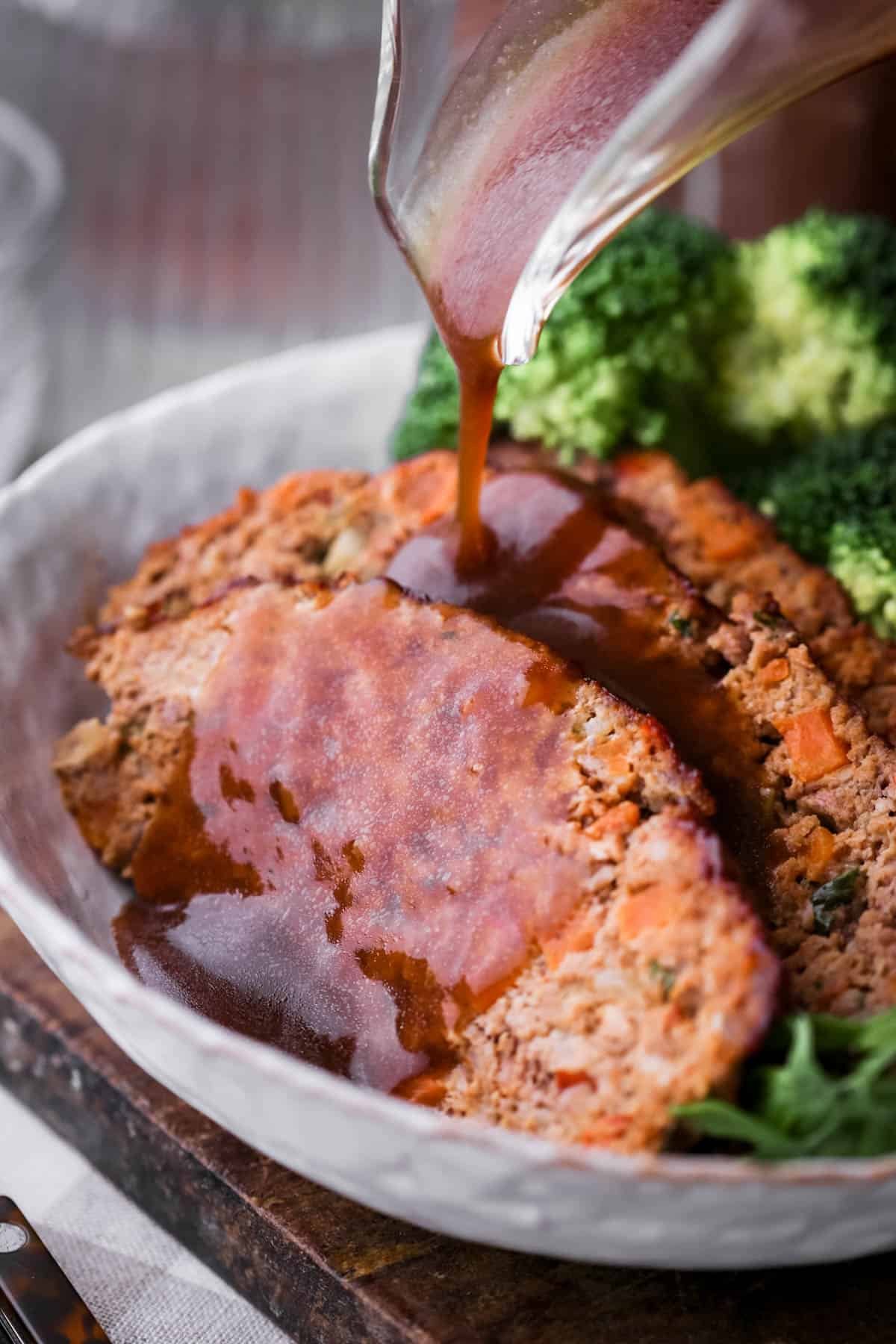 Rich gravy pouring over slices of meatloaf in a bowl.