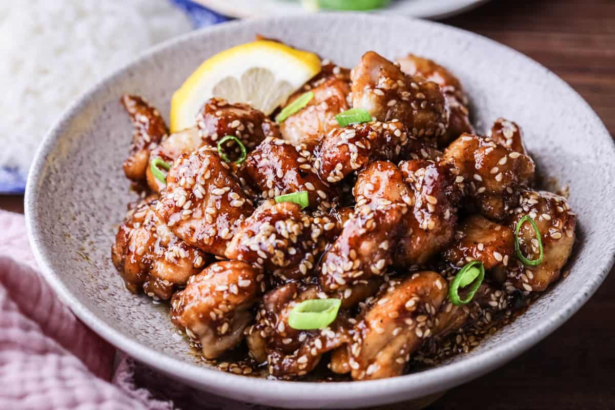 Sticky Lemon Chicken in a bowl with a slice of lemon and scattered with spring onions.