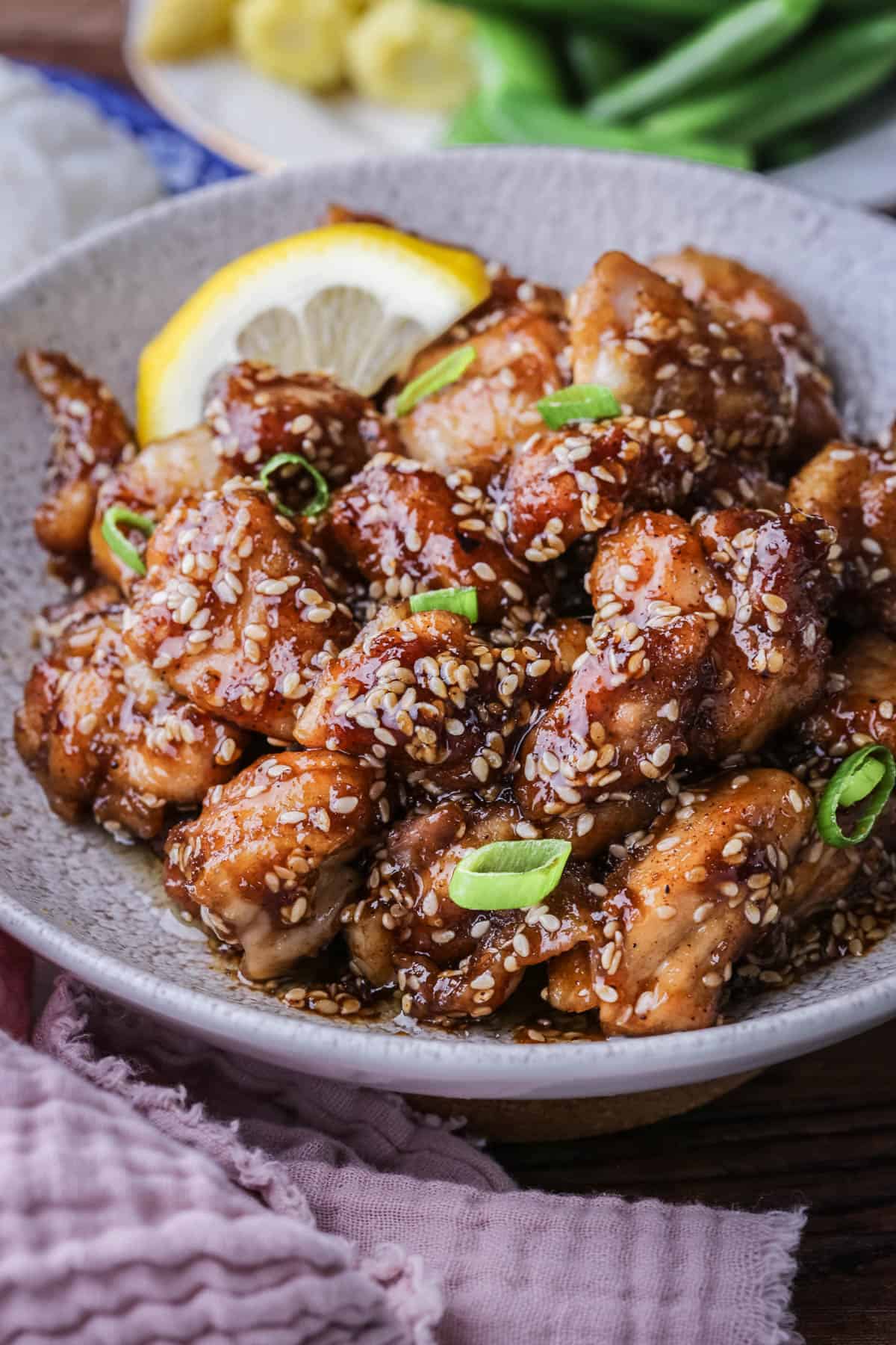 Sticky Lemon Chicken in a bowl with a slice of lemon and scattered with spring onions.