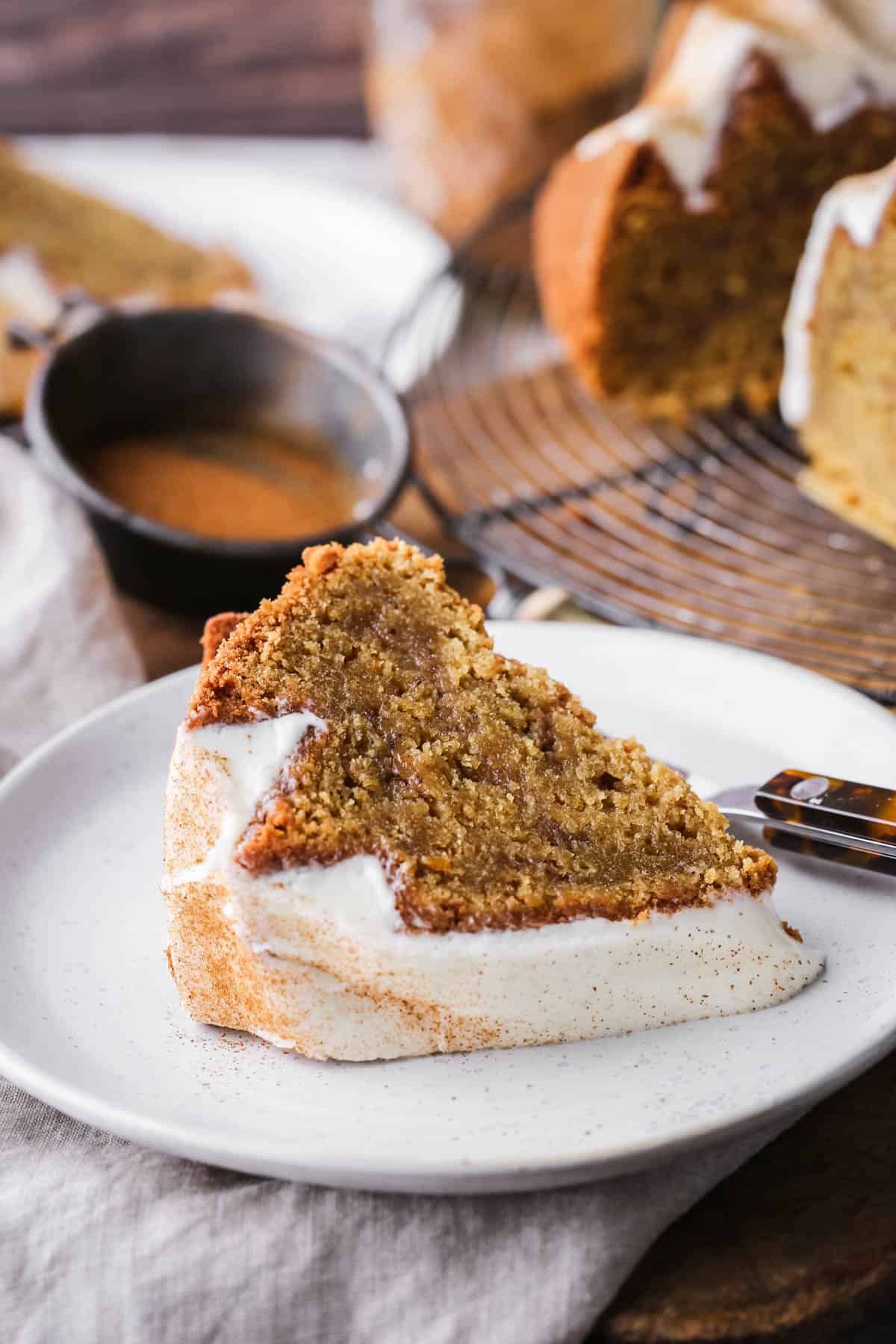 Slice of Sweet Potato Cake with sweet maple cream cheese icing and dusted with cinnamon. On a plate showing rich sponge inside with cinnamon swirl rippling through.