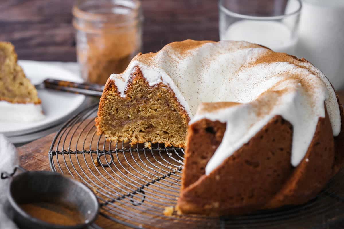 Sweet Potato Cake on wire rack covered in sweet maple cream cheese icing and dusted with cinnamon. Cut showing rich sponge inside with cinnamon swirl rippling through.