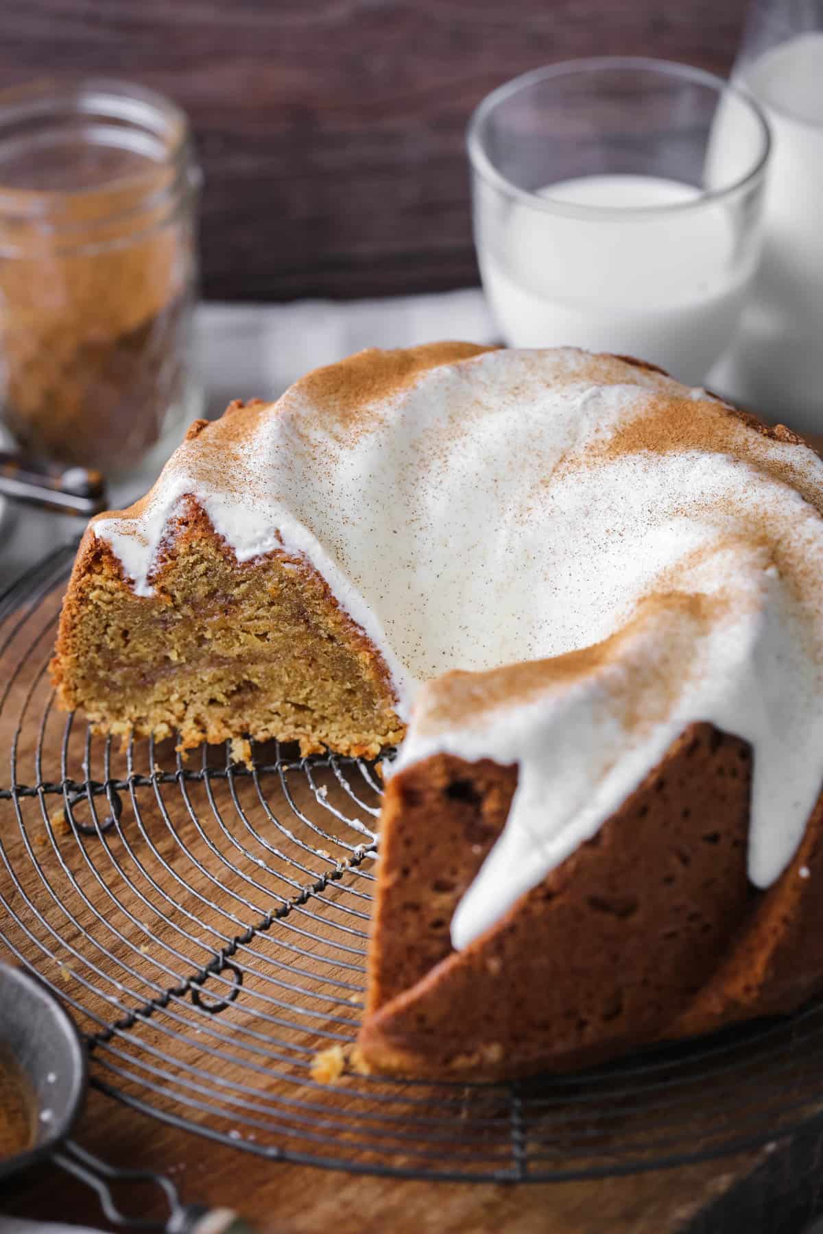 Sweet Potato Cake on wire rack covered in sweet maple cream cheese icing and dusted with cinnamon. Cut showing rich sponge inside with cinnamon swirl rippling through.
