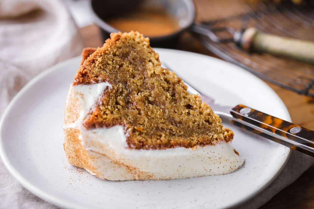 Slice of Sweet Potato Cake with sweet maple cream cheese icing and dusted with cinnamon. On a plate showing rich sponge inside with cinnamon swirl rippling through.