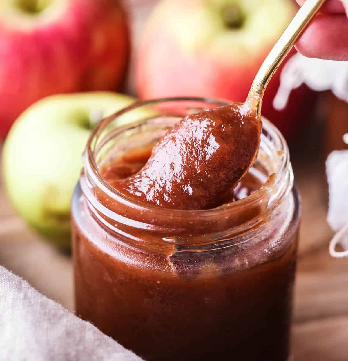 A spoon of richly glossy thick apple butter scooped out from jar.