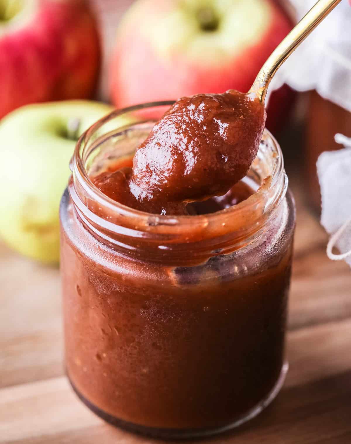 A spoon of richly glossy thick apple butter scooped out from jar.
