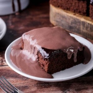 Smooth chocolate custard poured over a slice of chocolate cake showing it dripping down the sides.