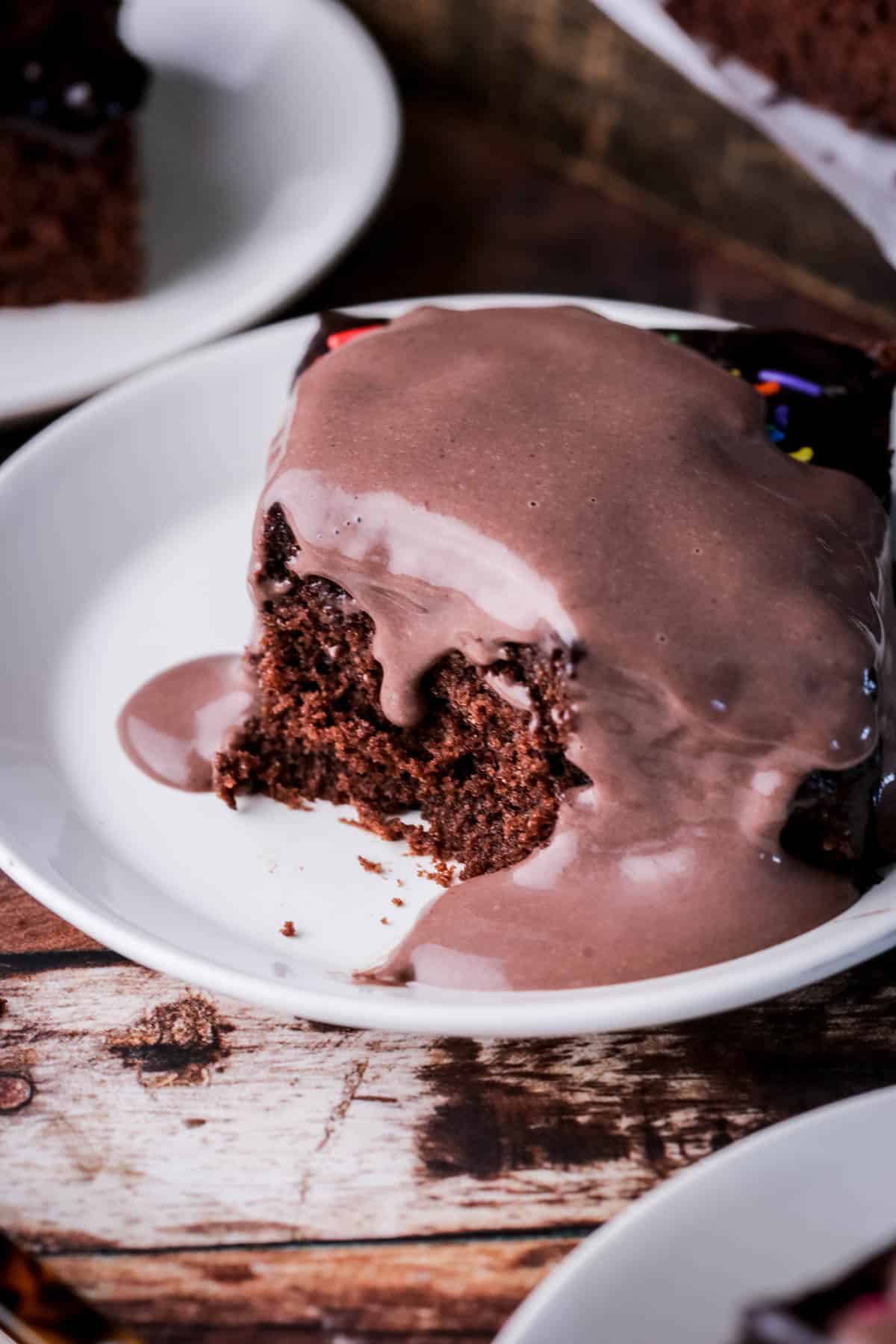Smooth chocolate custard poured over a slice of chocolate cake showing it dripping down the tender crumb.