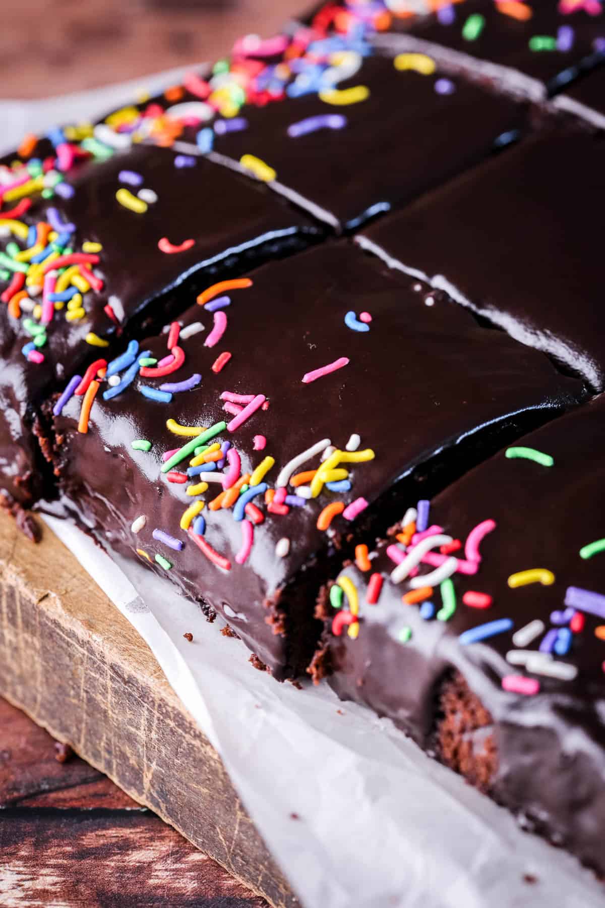 Chocolate School Cake topped with smooth chocolate icing and colourful sprinkles. Sliced into squares.