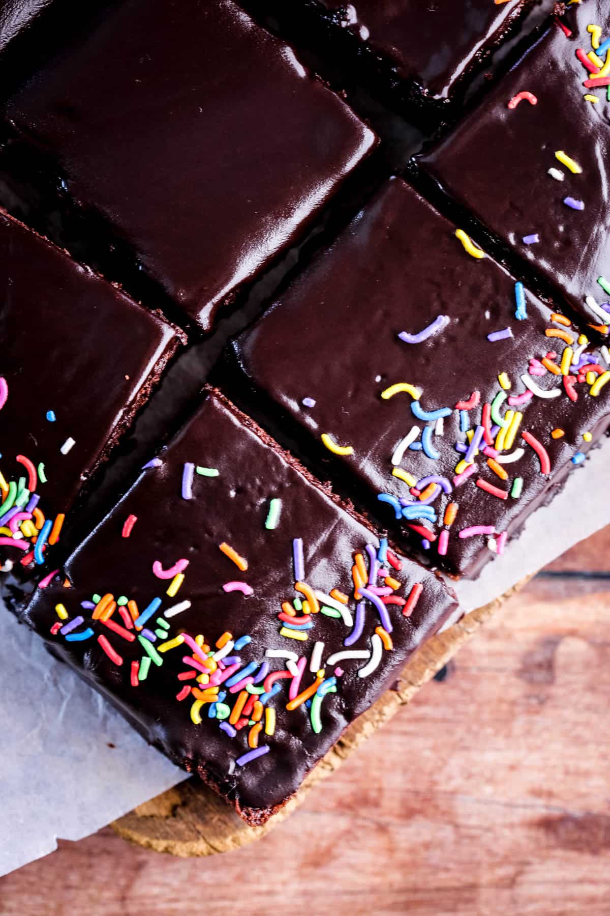 Chocolate School Cake topped with smooth chocolate icing and colourful sprinkles. Sliced into squares.