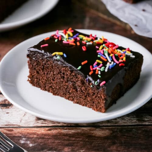 Slice of Chocolate School Cake topped with smooth chocolate icing and colourful sprinkles.