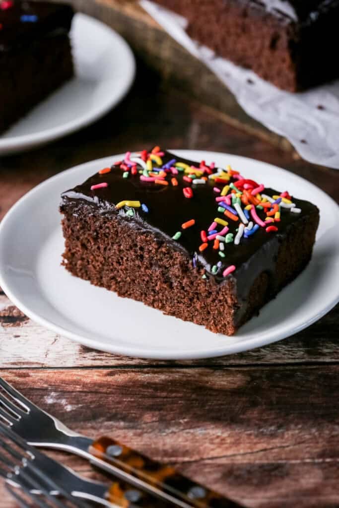 Slice of Chocolate School Cake topped with smooth chocolate icing and colourful sprinkles.