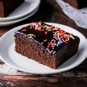 Slice of Chocolate School Cake topped with smooth chocolate icing and colourful sprinkles.