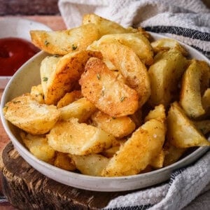 Homemade Crispy Gluten-Free Potato Wedges in a bowl with sprinkled sea salt and fresh thyme served with tomato ketchup.