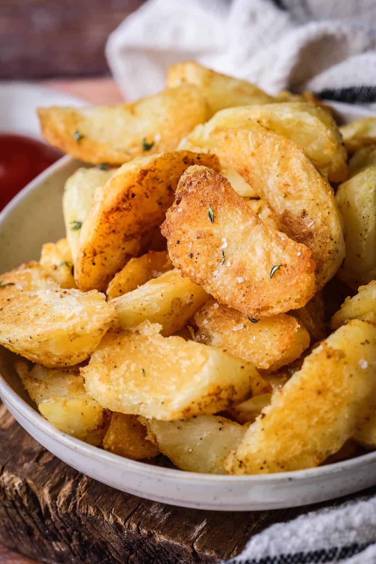 Homemade Crispy Gluten-Free Potato Wedges in a bowl with sprinkled sea salt and fresh thyme served with tomato ketchup.