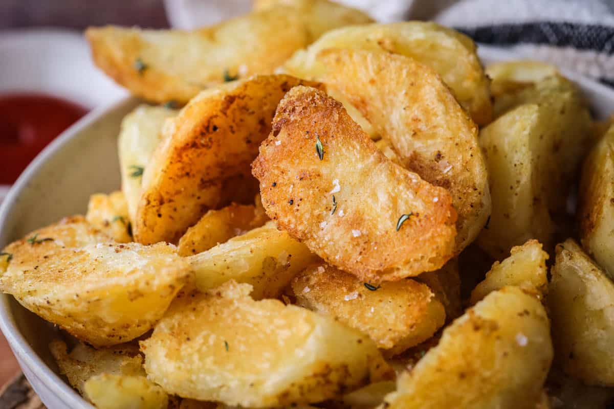 Homemade Crispy Gluten-Free Potato Wedges in a bowl with sprinkled sea salt and fresh thyme served with tomato ketchup.