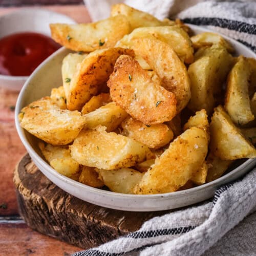 Homemade Crispy Gluten-Free Potato Wedges in a bowl with sprinkled sea salt and fresh thyme served with tomato ketchup.