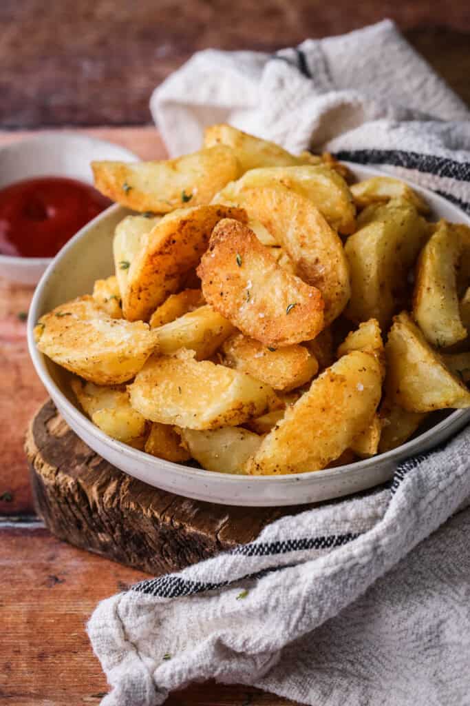 Homemade Crispy Gluten-Free Potato Wedges in a bowl with sprinkled sea salt and fresh thyme served with tomato ketchup.