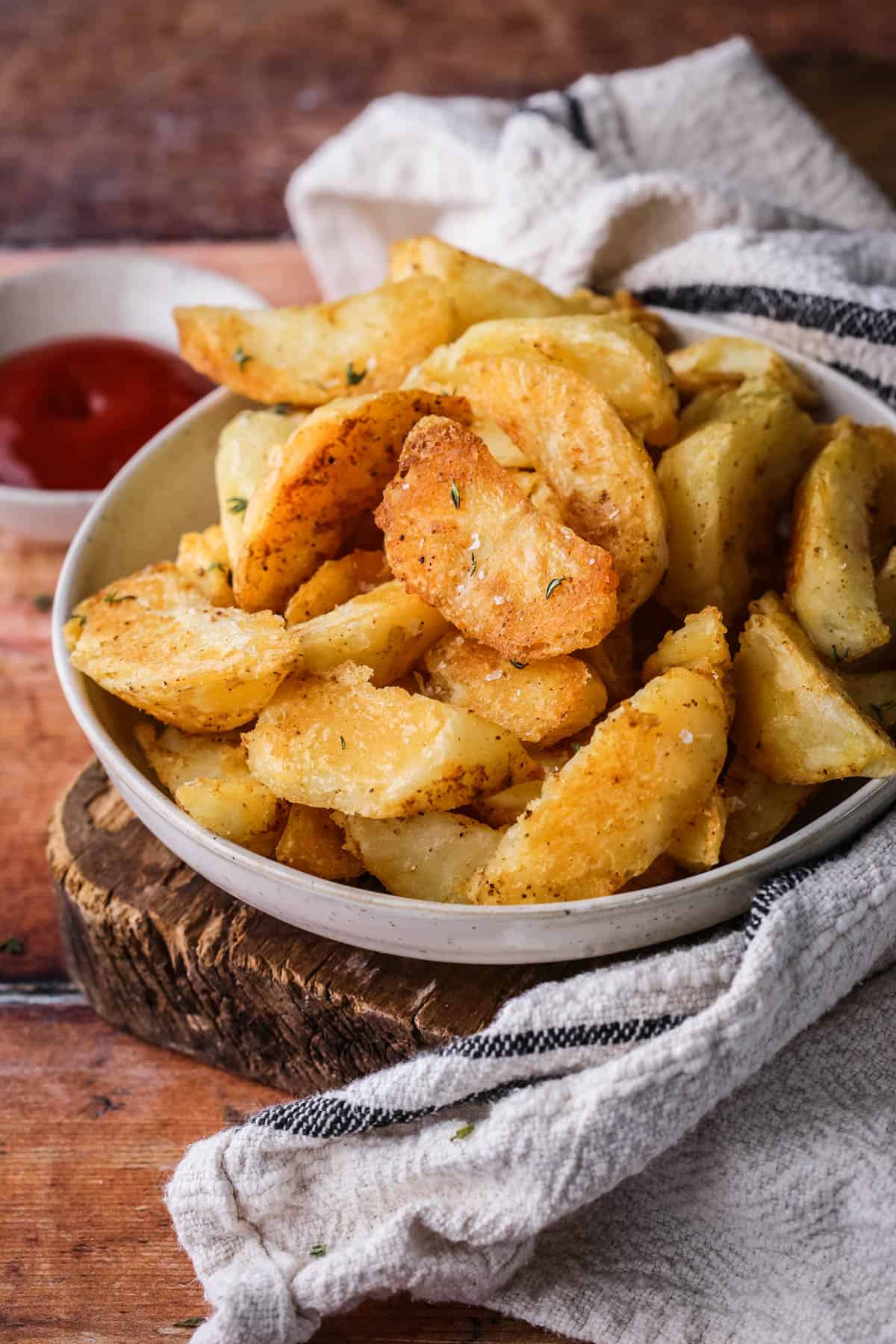 Homemade Crispy Gluten-Free Potato Wedges in a bowl with sprinkled sea salt and fresh thyme served with tomato ketchup.