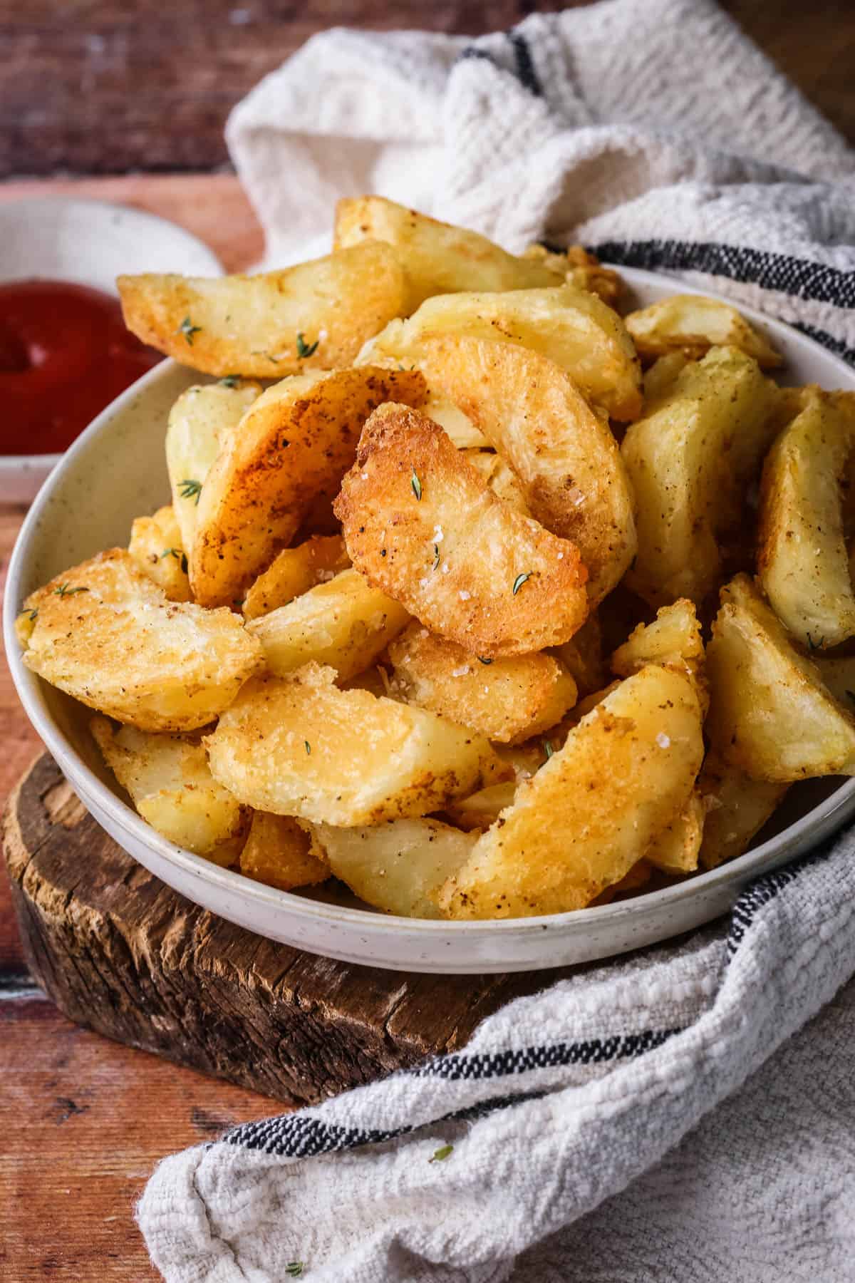 Homemade Crispy Gluten-Free Potato Wedges in a bowl with sprinkled sea salt and fresh thyme.