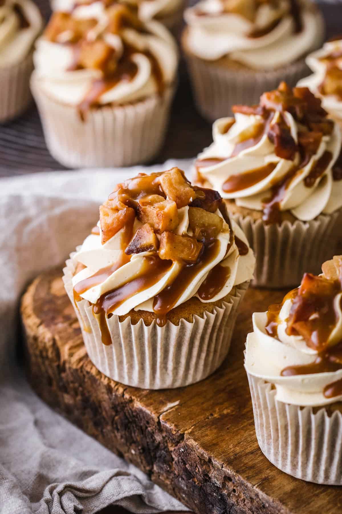 Sticky Toffee Apple Cupcake showing swirled creamy piping, topped with caramelised apples and drizzled with sticky toffee sauce.