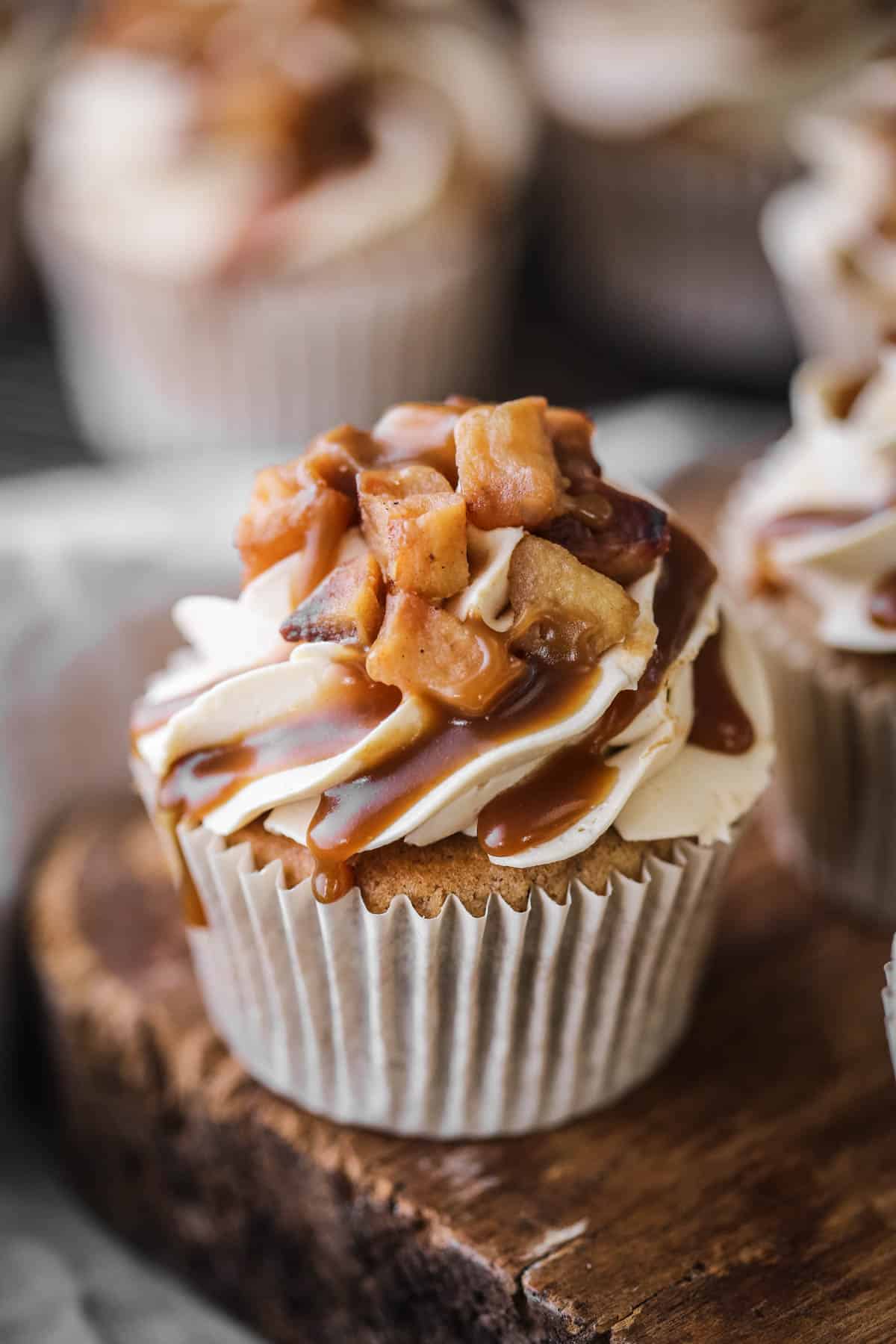 Sticky Toffee Apple Cupcake showing swirled creamy piping, topped with caramelised apples and drizzled with sticky toffee sauce.