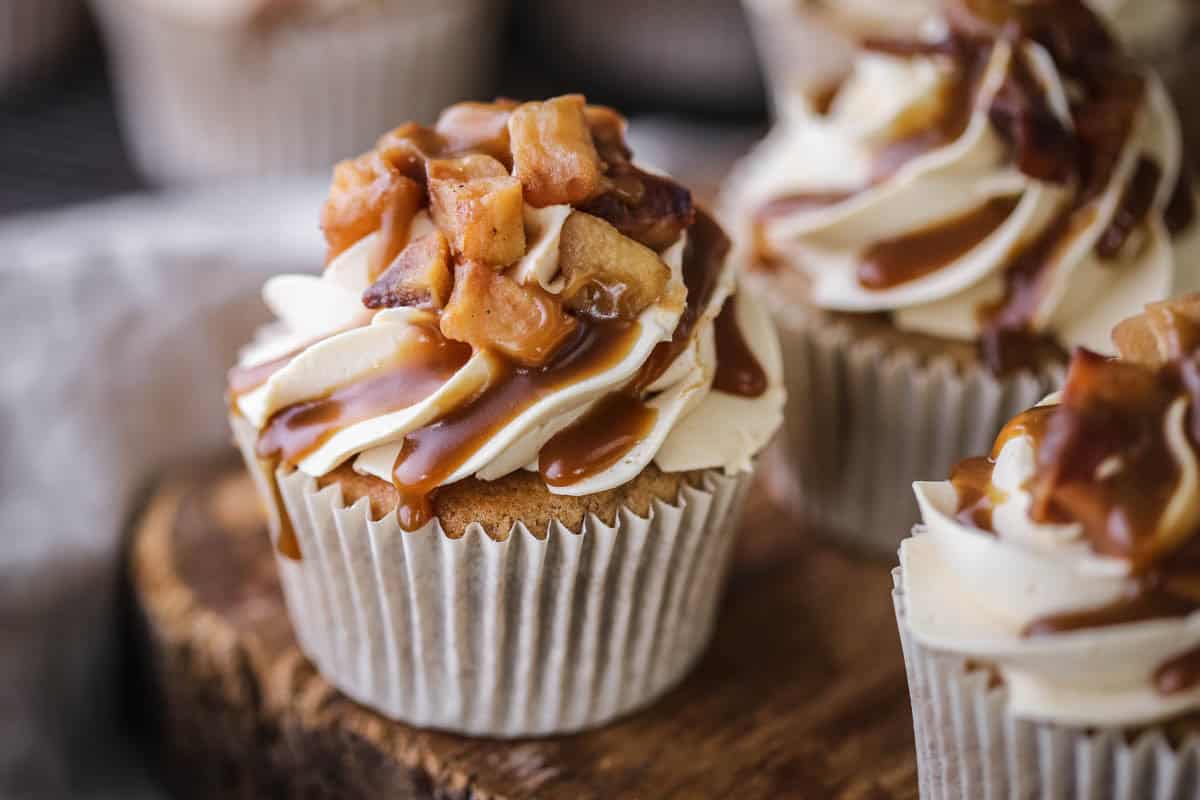 Sticky Toffee Apple Cupcakes showing swirled creamy piping, topped with caramelised apples and drizzled with sticky toffee sauce.
