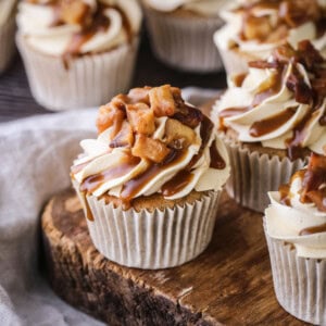 Sticky Toffee Apple Cupcakes showing swirled creamy piping, topped with caramelised apples and drizzled with sticky toffee sauce.