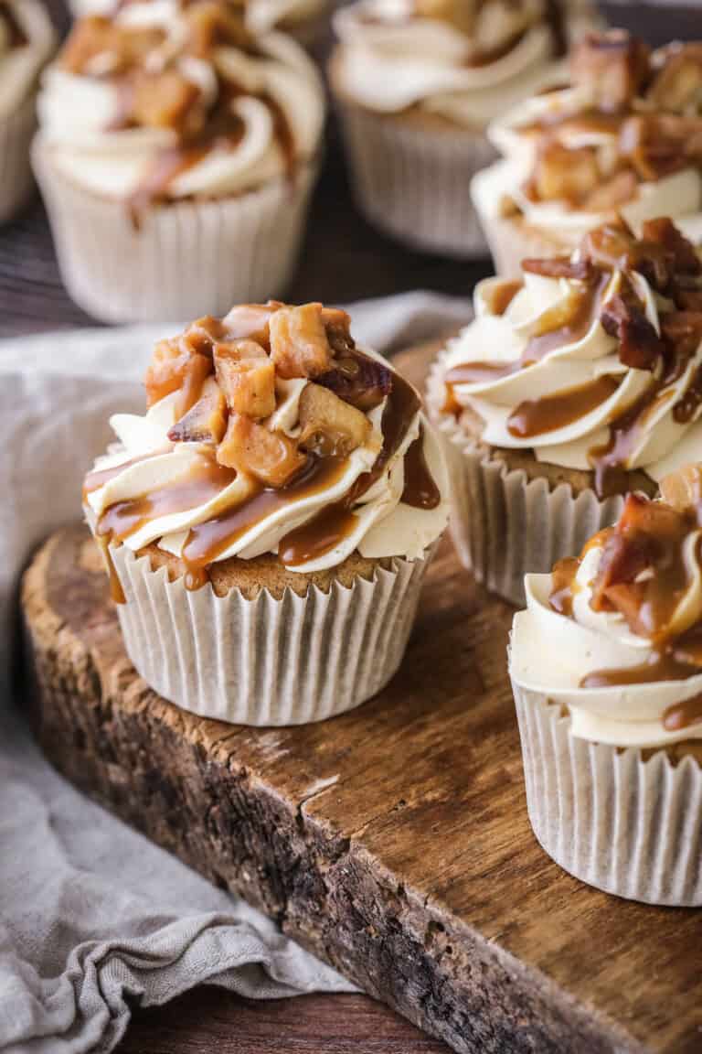 Sticky Toffee Apple Cupcakes showing swirled creamy piping, topped with caramelised apples and drizzled with sticky toffee sauce.