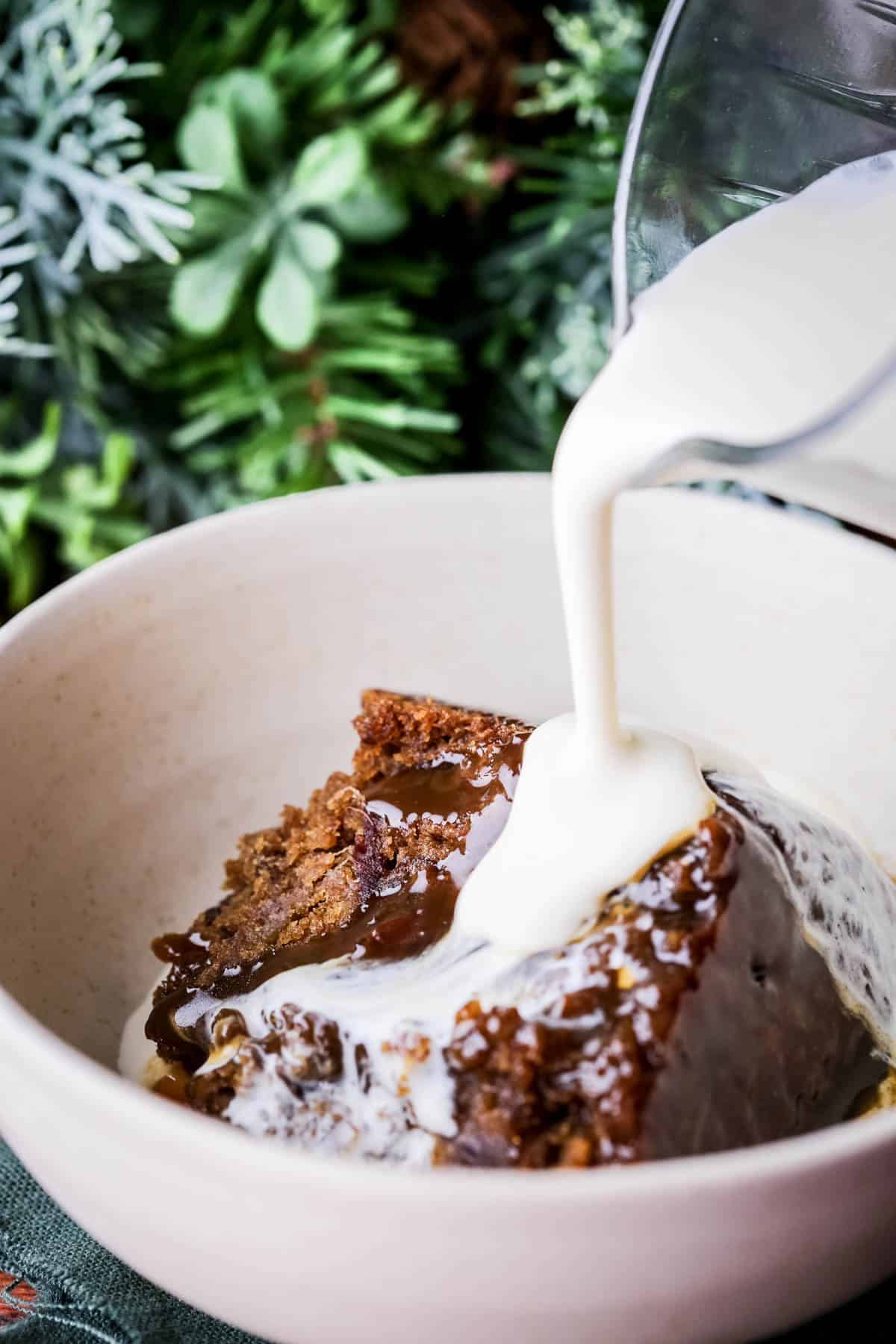 Sticky Toffee Christmas Pudding in a bowl with fresh cream poured over the top.