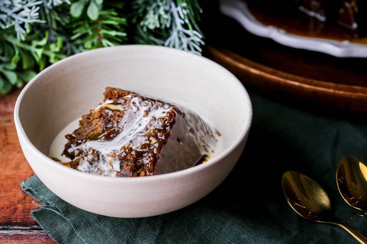 Sticky Toffee Christmas Pudding in a bowl with fresh cream poured over the top.