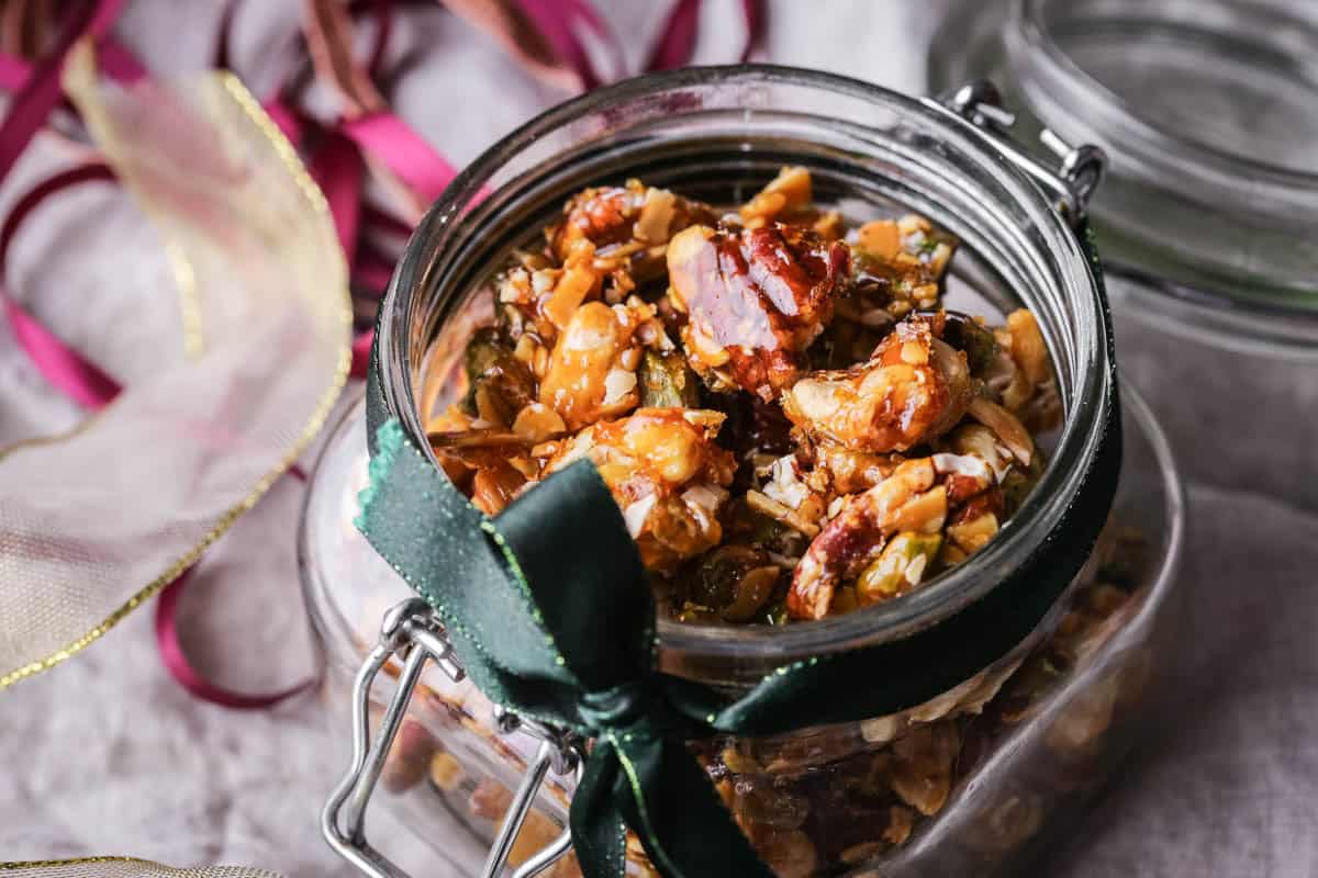 Caramelised Mixed Nuts in a glass jar wrapped with a festive ribbon.